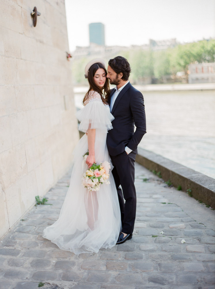 Couple in love posing during their romantic engagement session on Île Saint-Louis in Paris with the iconic Notre-Dame Cathedral in the background