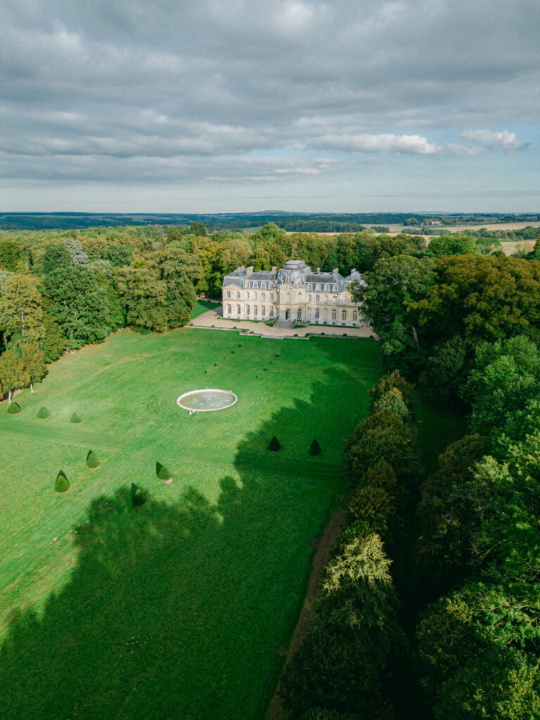 Overhead, the Château de Champlatreux sits like a jewel amidst verdant landscapes, epitomizing luxury wedding châteaux near Paris, an idyllic setting for a fairy-tale wedding