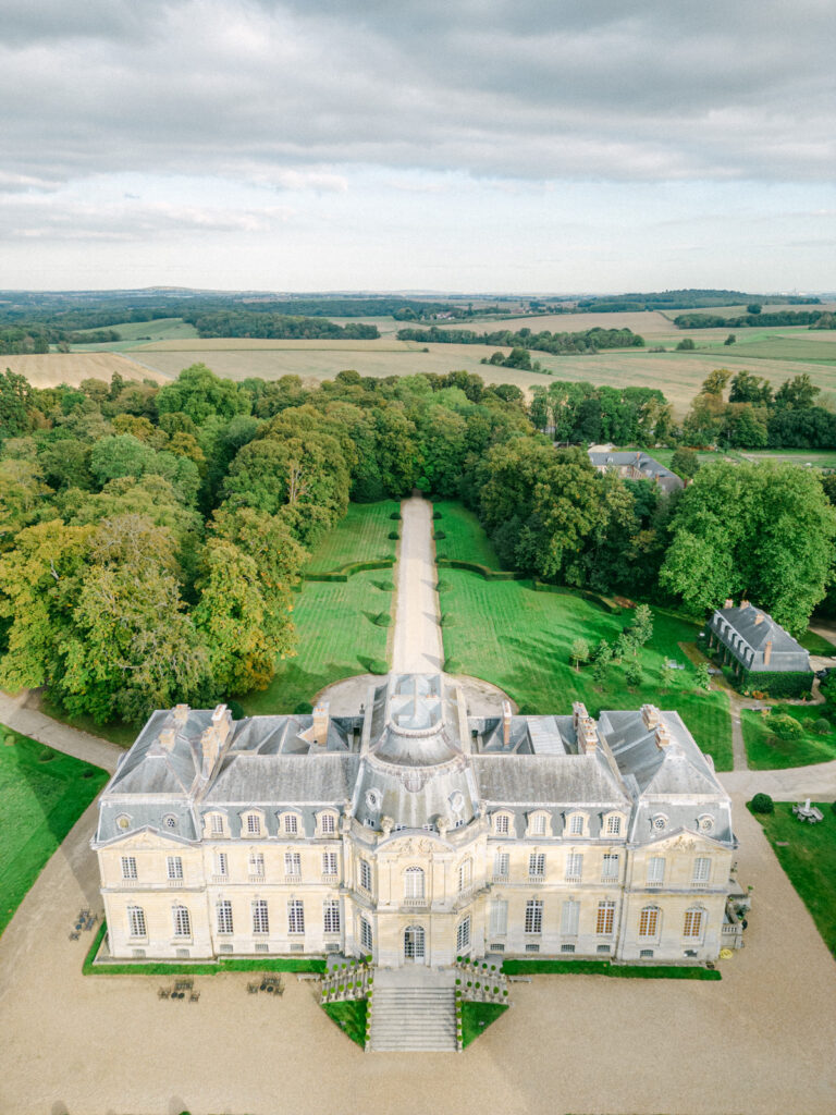 Overhead, the Château de Champlatreux sits like a jewel amidst verdant landscapes, epitomizing luxury wedding châteaux near Paris, an idyllic setting for a fairy-tale wedding