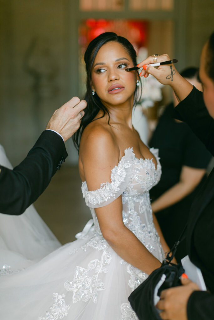Under the serene skies of Chateau de Villette, the bride’s makeup is gracefully perfected, echoing the elegance of her Parisian outdoor wedding.