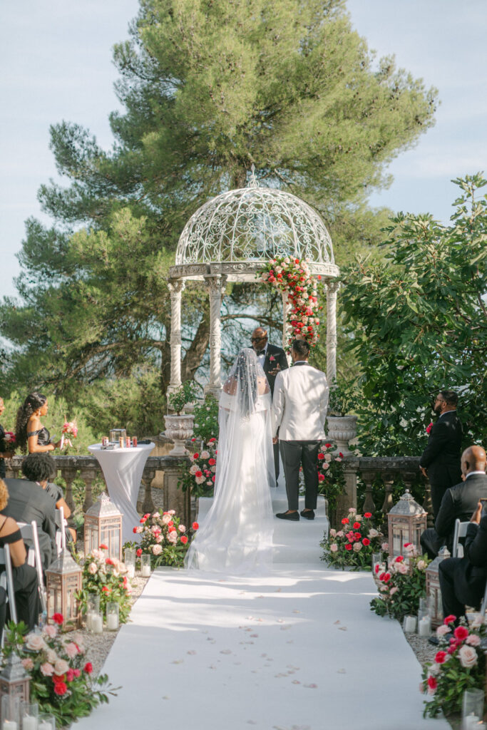 Couple exchanging vows under a floral arch at Château Saint-Georges, with guests and the Riviera's landscape in the background, epitomizing their French-Riviera-St-Georges-Wedding