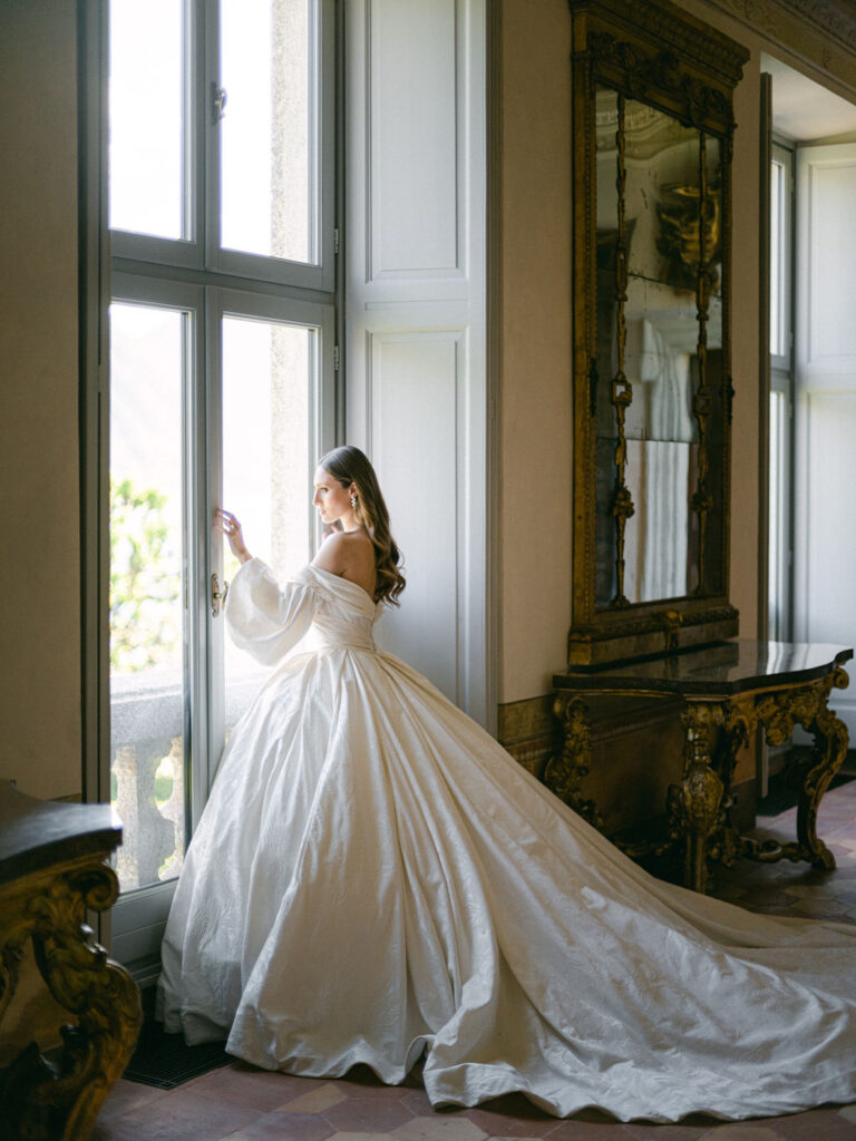 A solitary moment as the bride reflects by Lake Como, her silhouette framed by the natural beauty ideal for a Luxury Balbiano Wedding