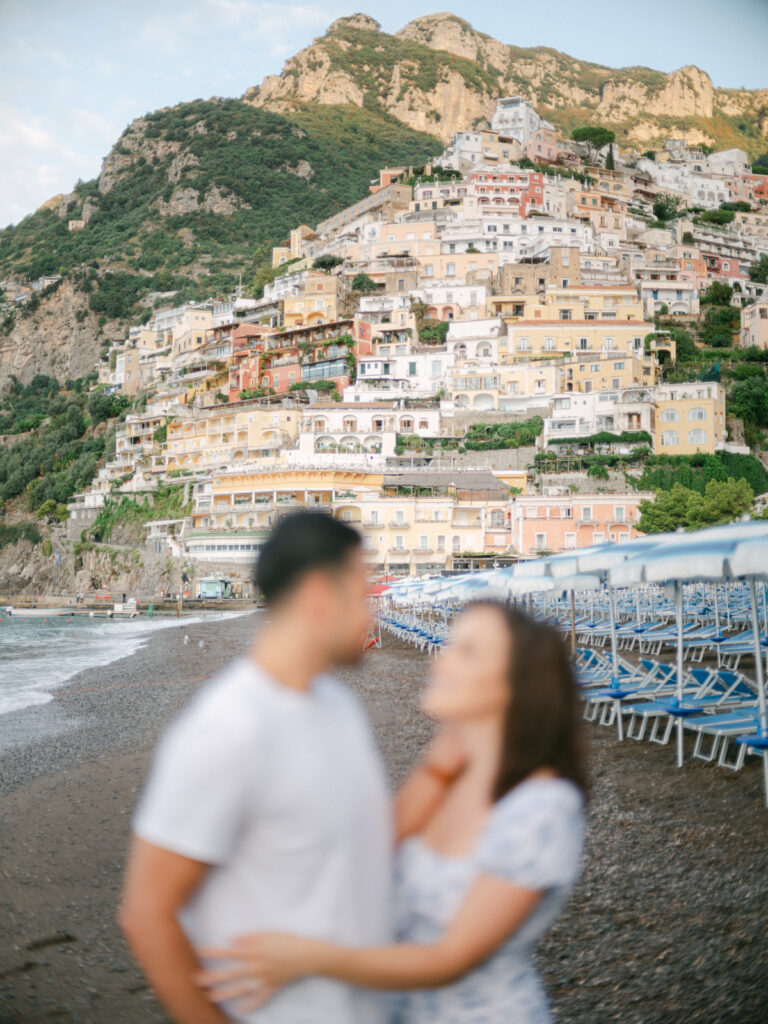 Honeymoon in Positano: A couple embraces on a sun-drenched terrace, with the colorful cliffs of Positano and the sparkling Mediterranean in the background.